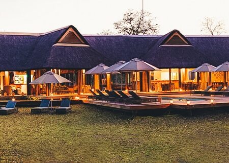 Lodge de luxe éclairé au crépuscule avec terrasse et piscine.